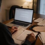 Πολίτης χρησιμοποιεί laptop και εξετάζει έγγραφα για ηλεκτρονική υποβολή ανώνυμης ή επώνυμης καταγγελίας στην ΑΑΔΕ.